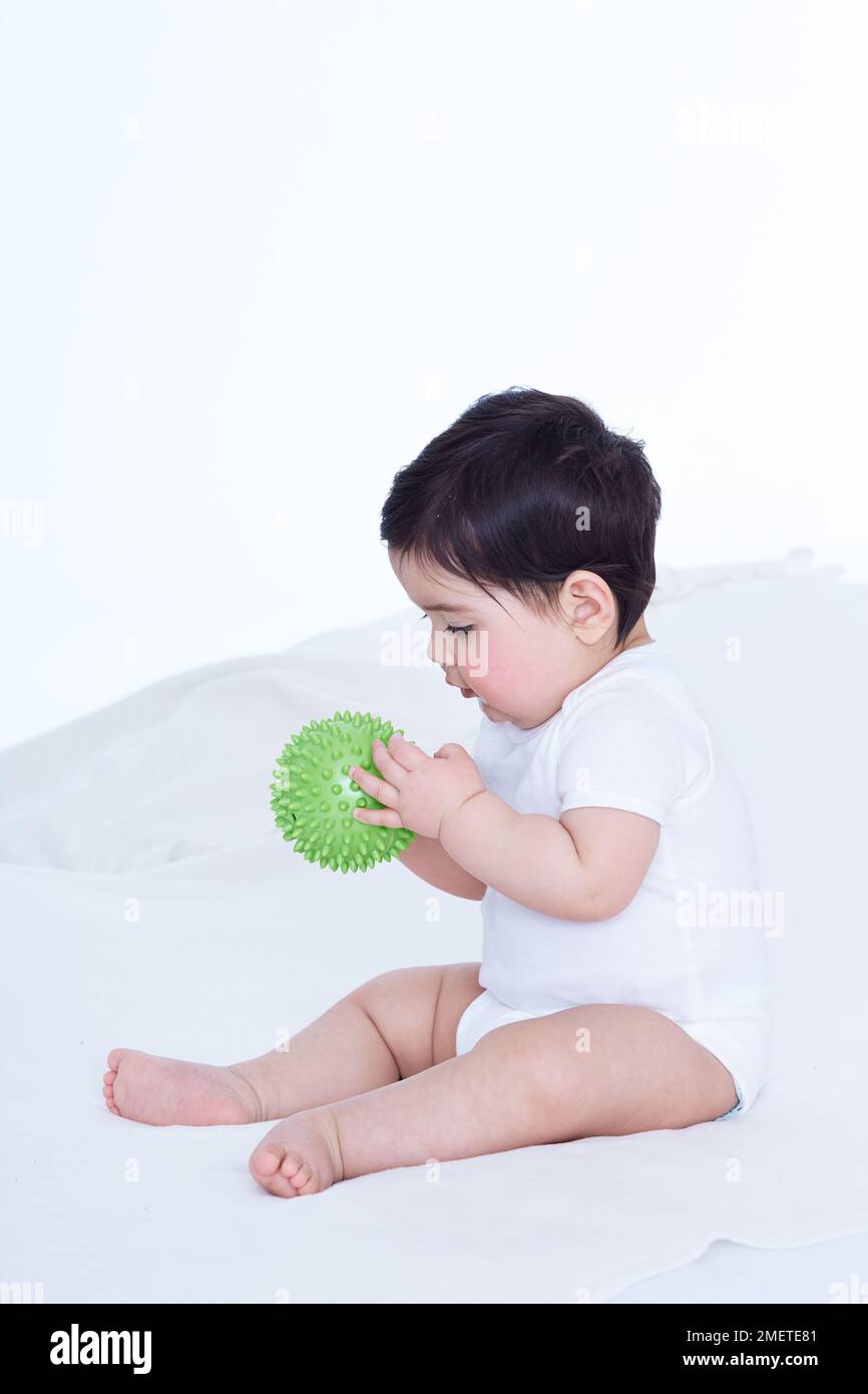 Bebé niña (40 semanas) tocando pelota de goma Foto de stock