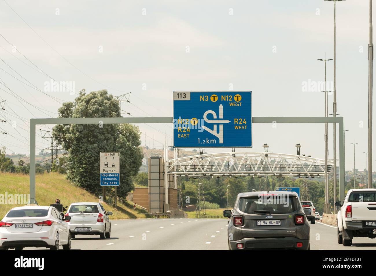 Señales azules de autopistas y automóviles, tráfico en una carretera de peaje justo antes de viajar bajo un pórtico para recoger peajes en Gauteng, Sudáfrica Foto de stock