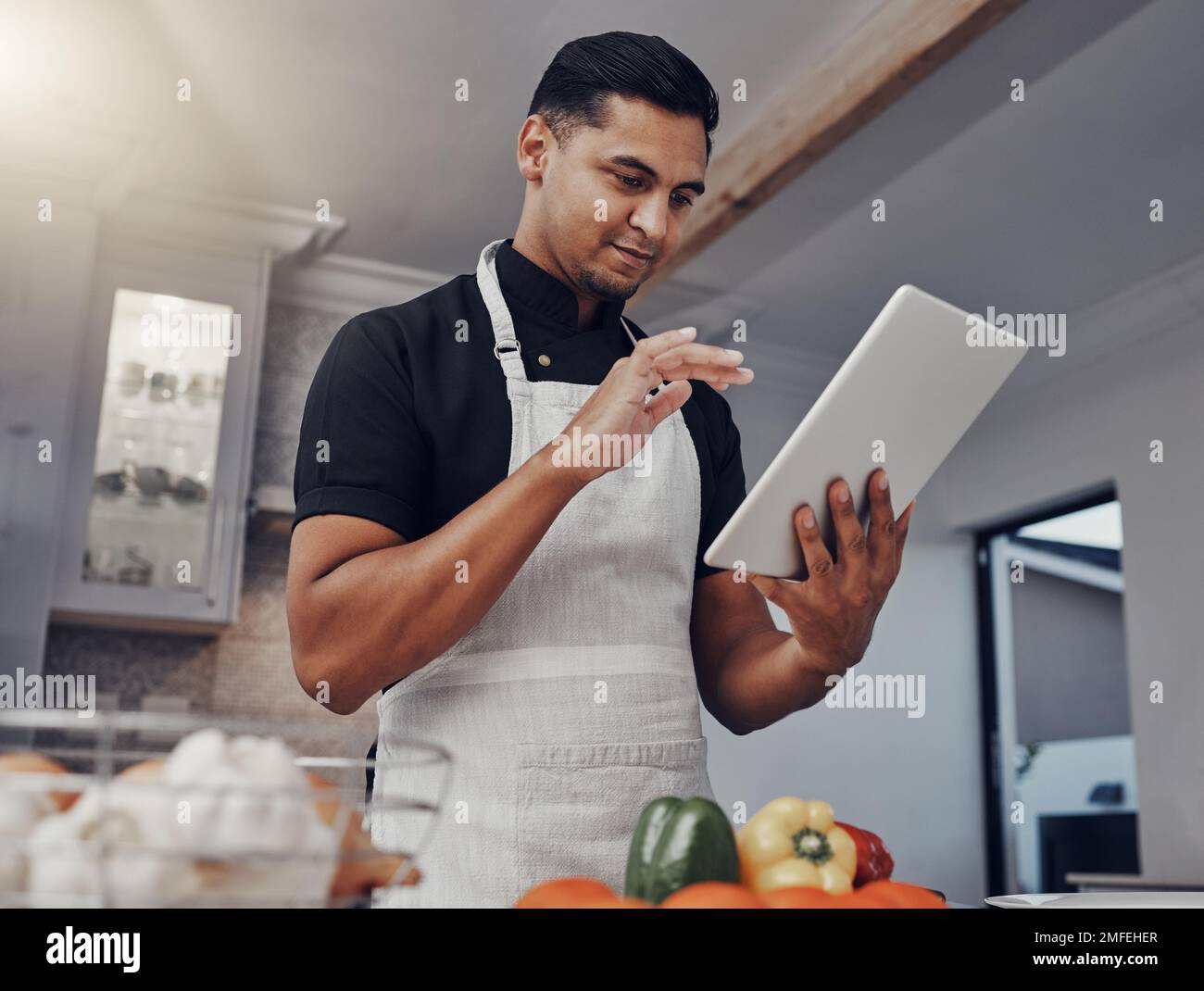 Hombre, cocinar verduras y tableta en la cocina mientras está en línea con la conexión wifi de la casa para el aprendizaje o el blog. Chef persona con aplicación móvil para online Foto de stock