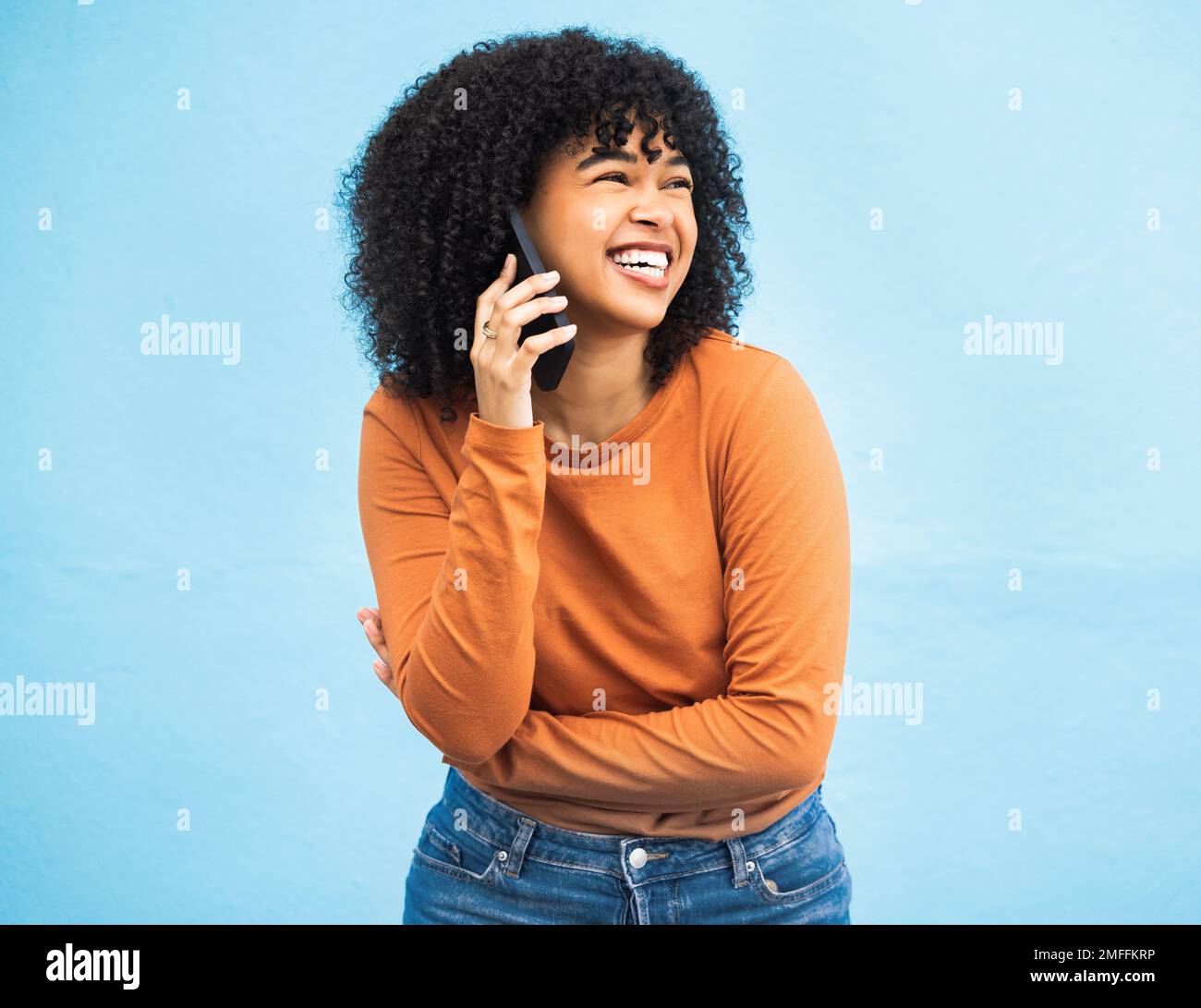 Mujer negra riendo, afro y llamada telefónica en fondo azul aislado para chismes divertidos, noticias de comedia o historia cómica. Sonríe, feliz y estudiante hablando Foto de stock
