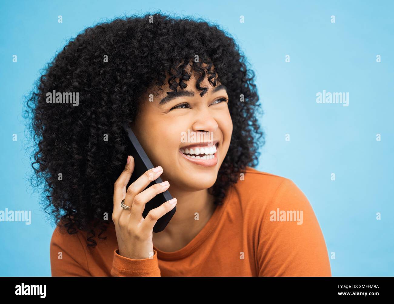 Mujer negra riendo, cara y llamada telefónica por fondo azul aislado en chismes divertidos, noticias e historia cómica. Sonríe, afro y persona feliz hablando Foto de stock