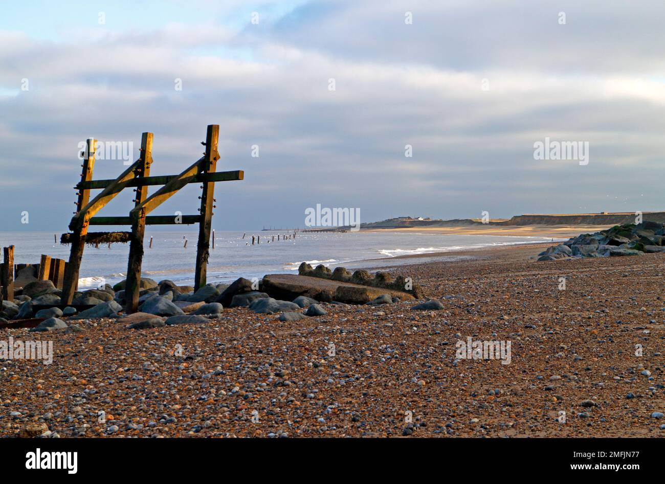 Una vista a lo largo de la playa con viejas defensas marinas abandonadas en invierno en aguas bajas en la costa de Norfolk en Happisburgh, Norfolk, Inglaterra, Reino Unido. Foto de stock