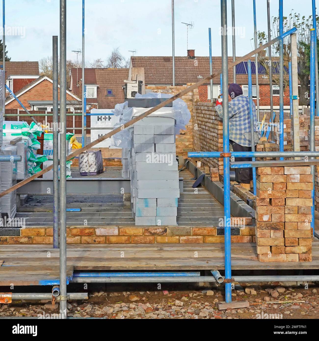 Albañil trabajando entre andamios y materiales de construcción Etapas tempranas de la estructura de pared de la cavidad de ladrillo de la nueva casa unifamiliar Inglaterra Reino Unido Foto de stock