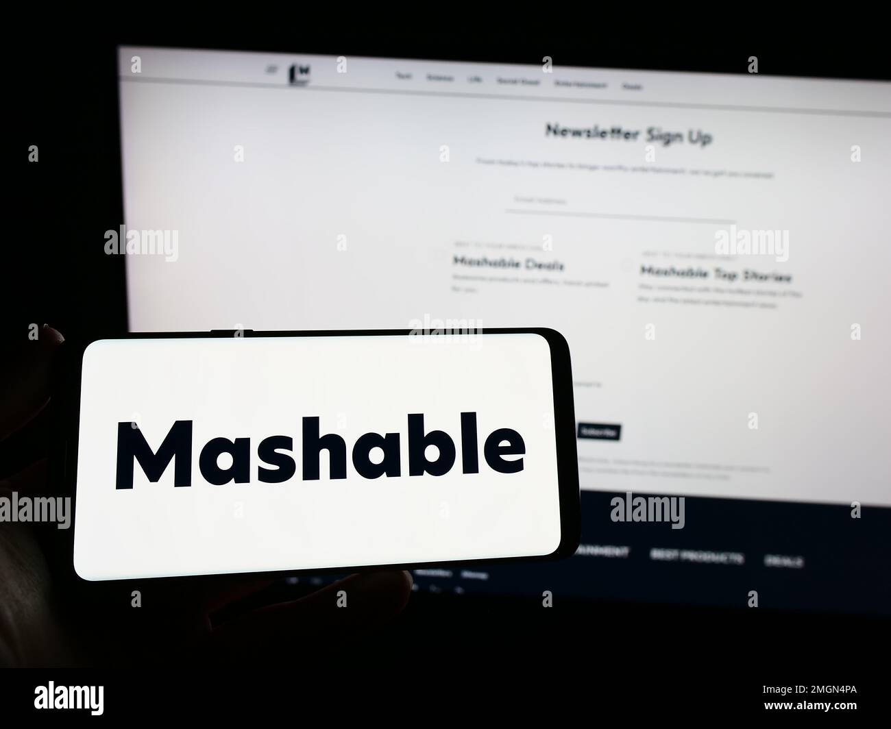 Persona que sostiene el teléfono móvil con el logotipo de la compañía de medios  digitales estadounidense Mashable en la pantalla delante de la página web  del negocio. Enfoque en la pantalla del