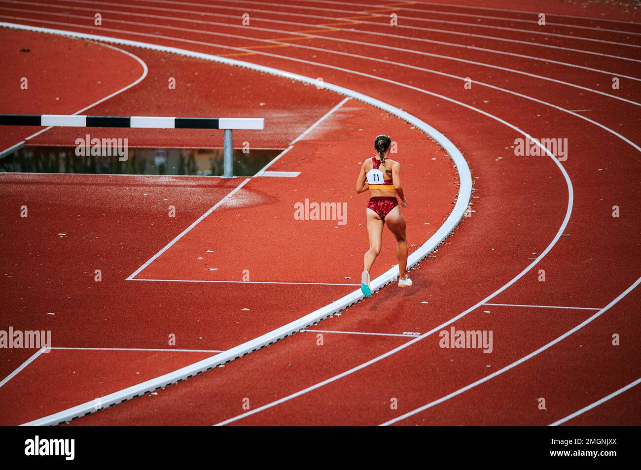 Atleta femenina decidida en medio de una carrera de distancia en la pista. Perfecto para promover la perseverancia, el atletismo y la aptitud física Foto de stock