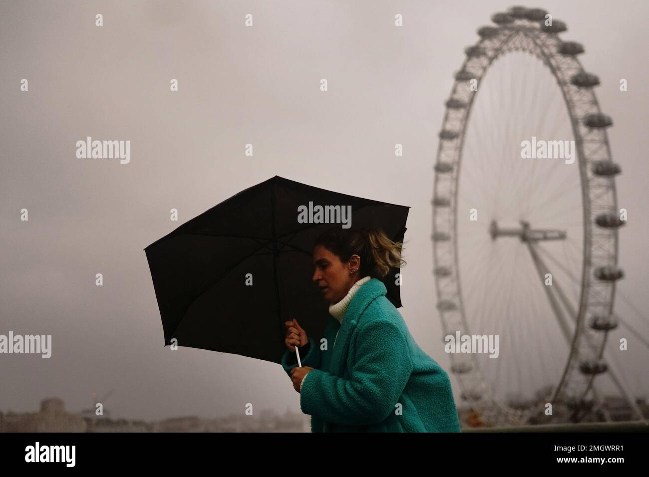 Una mujer se cubre contra el clima húmedo y ventoso en el puente de Westminster en el centro de Londres. Fecha de la fotografía: Jueves 26 de enero de 2023. Foto de stock