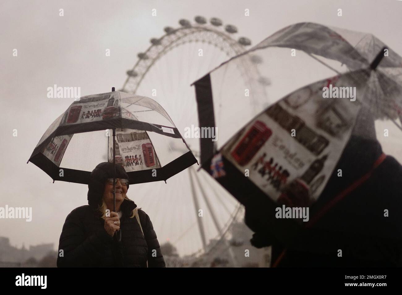Dos turistas se encubren contra el clima húmedo y ventoso en el puente de Westminster en el centro de Londres. Fecha de la fotografía: Jueves 26 de enero de 2023. Foto de stock