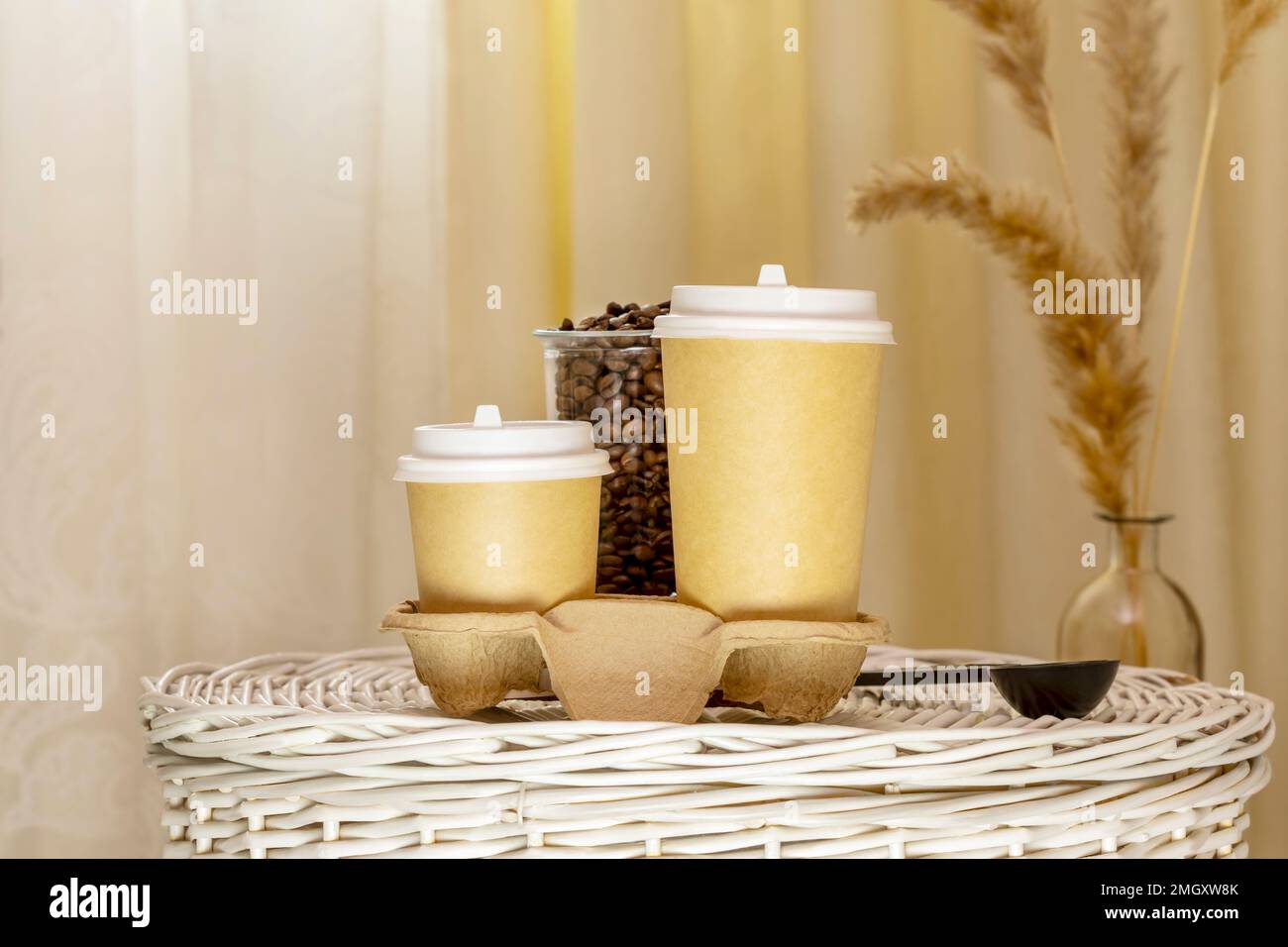 Café para llevar. Composición de café con dos tazas de cartón ecológicas desechables en la cesta de mimbre en el interior ligero con flores secas. Café para llevar Foto de stock