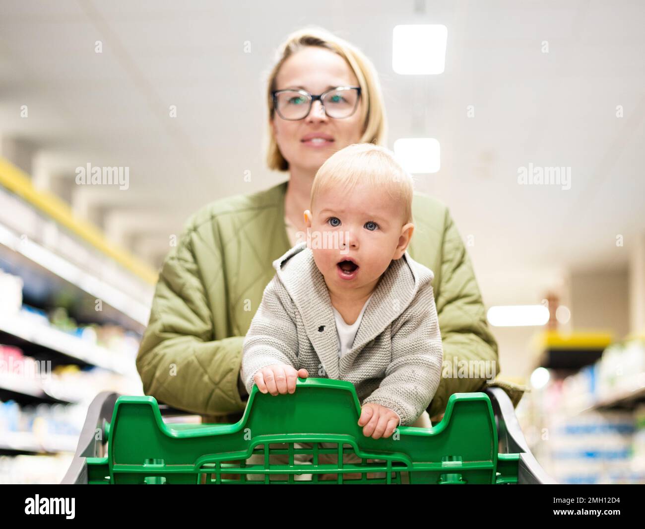 Madre empujando el carrito de compras con su bebé niño niño pequeño pasillo del departamento en supermercado supermercado tienda de comestibles. Compras con el concepto de los niños Foto de stock