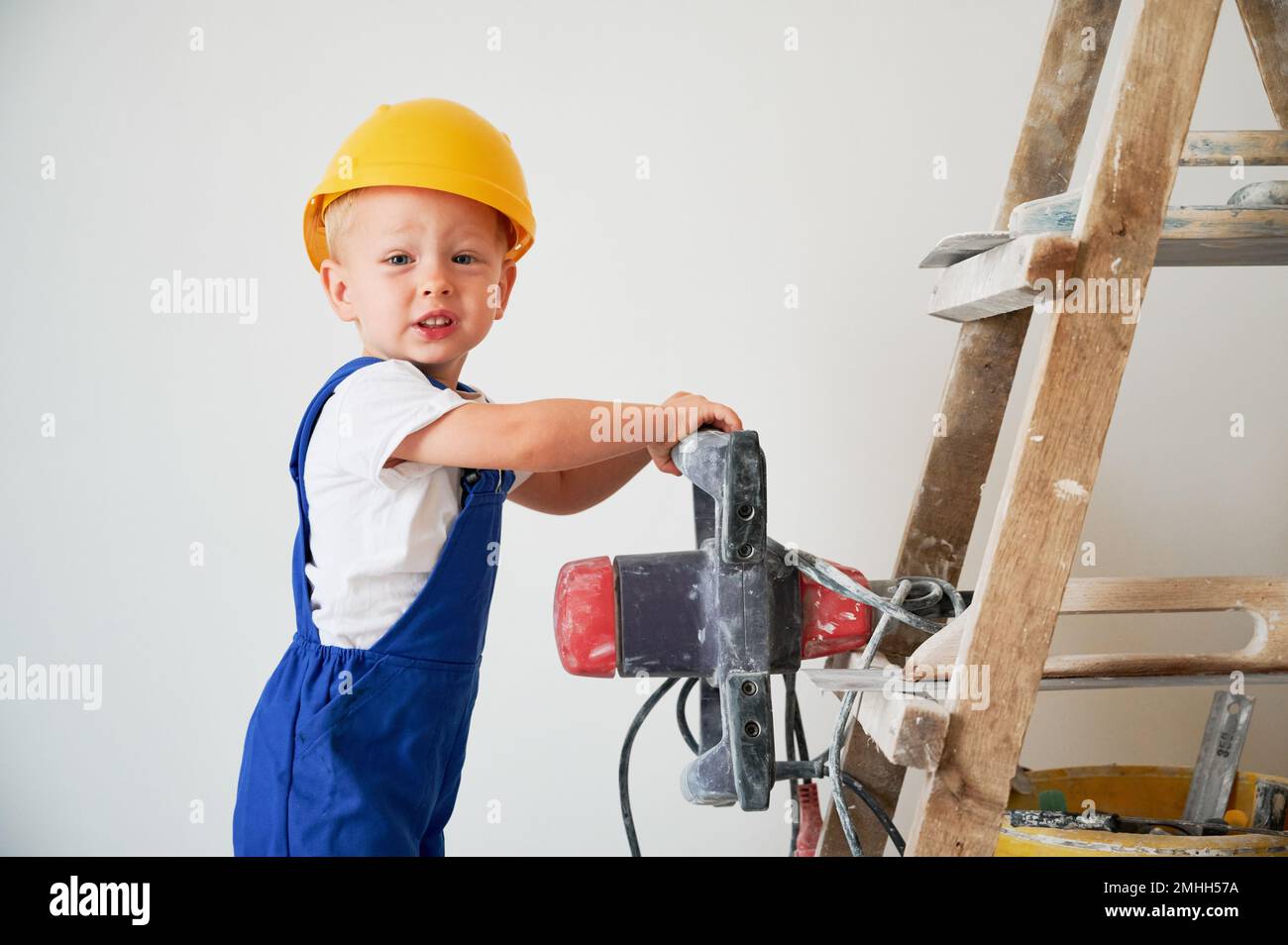 Pequeño trabajador de la construcción del muchacho que mide la superficie  de la pared con la herramienta del nivel del espíritu. Niño en mono de  trabajo usando instrumento de nivel de burbuja