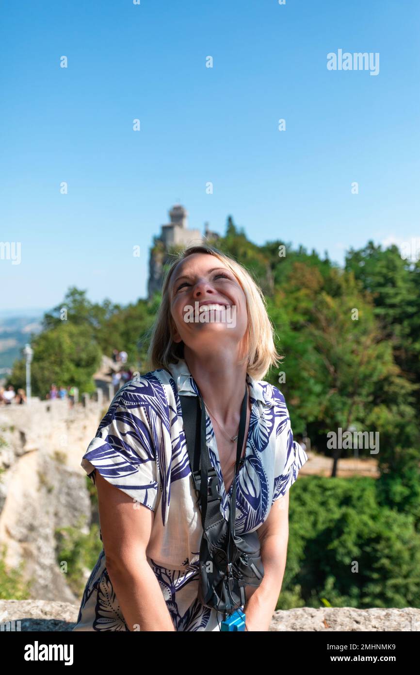Joven mujer hermosa sonríe en el telón de fondo de la Fortaleza Guaita, San Marino, Italia Foto de stock