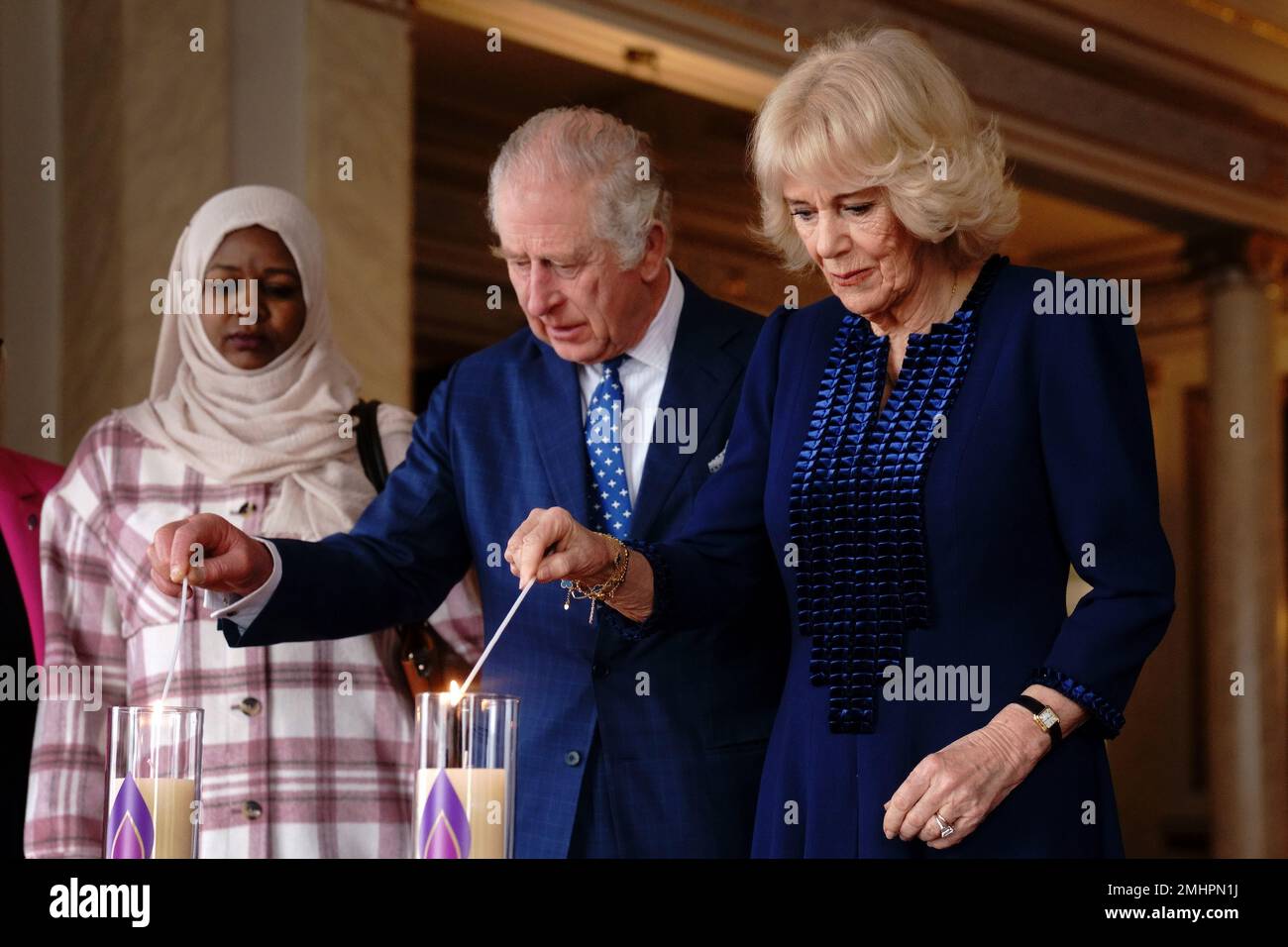El rey Carlos III y la Reina consorte encienden una vela en el Palacio de Buckingham, Londres, para conmemorar el Día de los Caídos del Holocausto, junto a Amouna Adam, sobreviviente del genocidio de Darfur, y el sobreviviente del Holocausto Dr. Martin Stern (no en la foto). Fecha de la fotografía: Viernes 27 de enero de 2023. Foto de stock