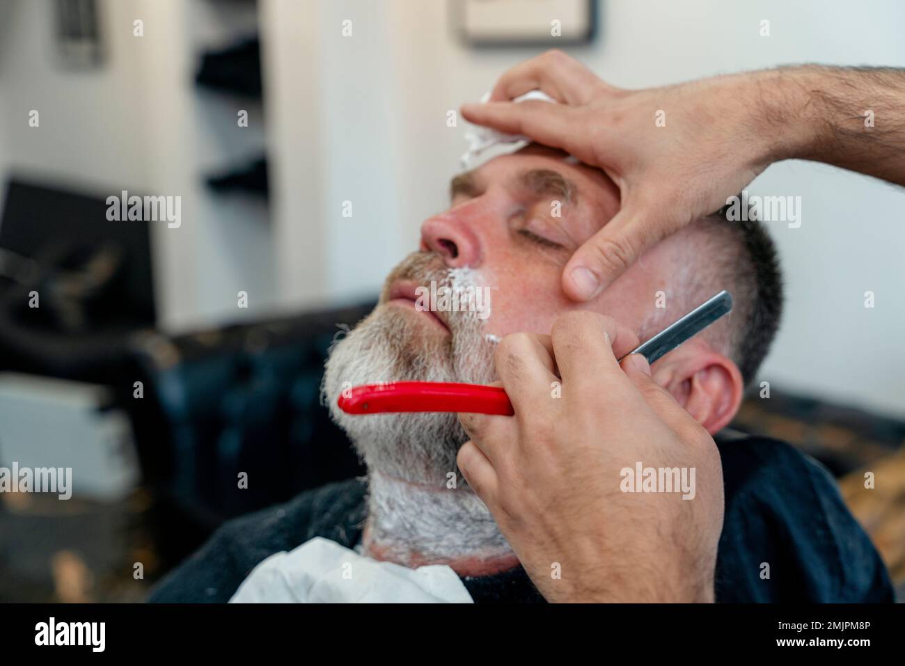 Peluquero tatuado recortando al hombre barbudo con máquina de