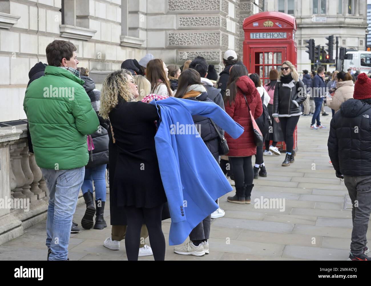 Londres, Inglaterra, Reino Unido. Los turistas hacen cola para hacerse una foto en uno de los icónicos teléfonos rojos de Parliament Square, Westminster. Foto de stock