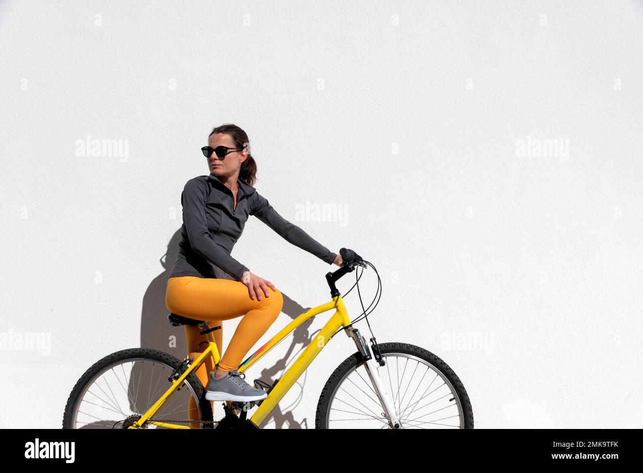 mujer montando una bicicleta mirando sobre su hombro, fondo blanco de la pared con copyspace. Foto de stock