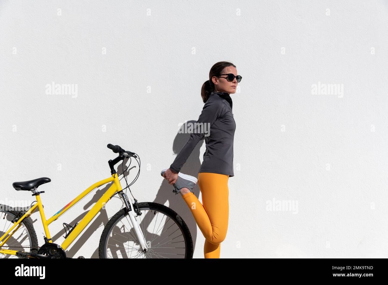 mujer ciclista de pie haciendo un estiramiento de pierna Foto de stock