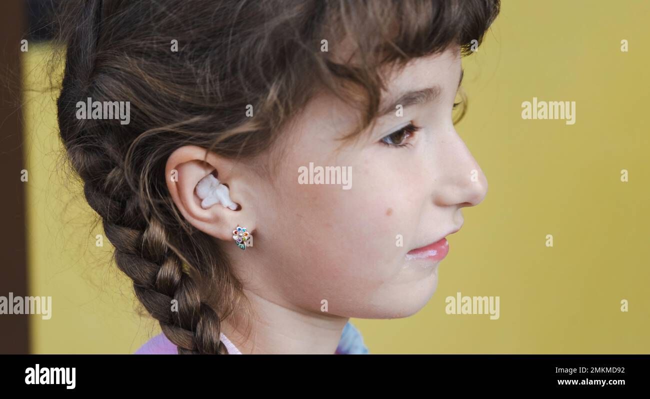 Chica con un hisopo de algodón terapéutico caliente en la oreja con una cara  triste y llorosa está sosteniendo su oreja. Dolor de oído, otitis media,  hinchazón de mejillas, encías Fotografía de