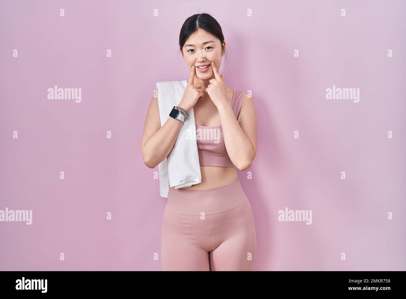Mujer joven china con ropa deportiva y sonriendo con la boca abierta, los dedos apuntando y forzando una sonrisa Fotografía de stock -