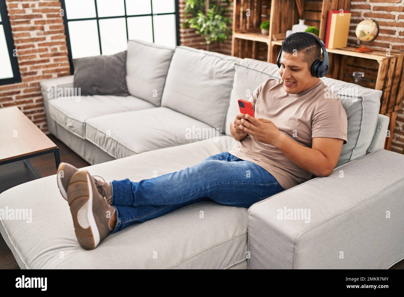 Joven latino escuchando música sentado en el sofá de la casa Fotografía de  stock - Alamy