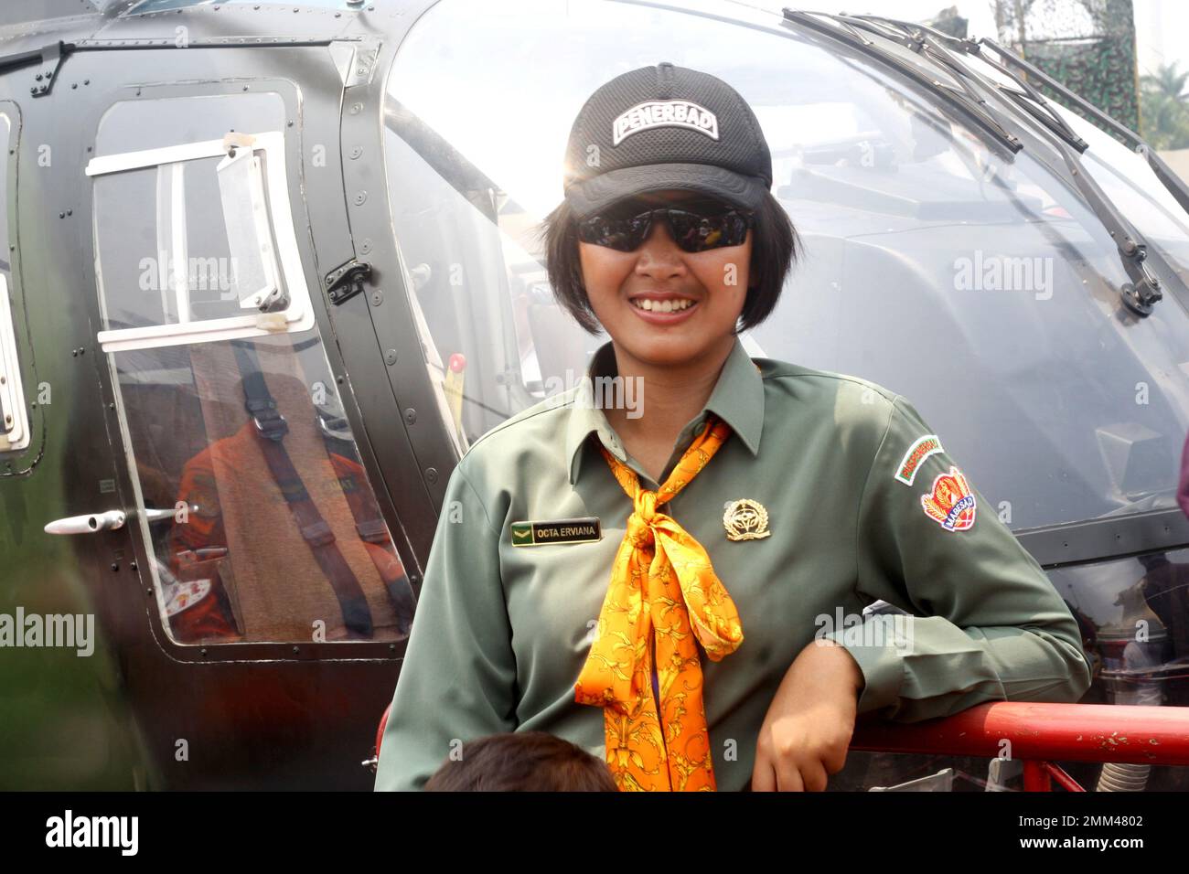 Retrato de una piloto del ejército indonesio, lleva gafas de sol, sonríe a la cámara y posa frente al helicóptero. Foto de stock