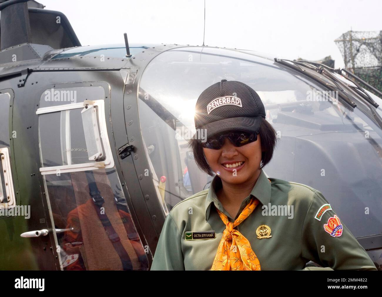 Retrato de una piloto del ejército indonesio, lleva gafas de sol, sonríe a la cámara y posa frente al helicóptero. Foto de stock