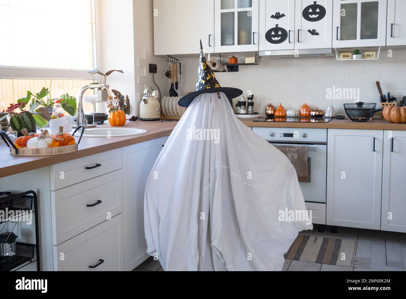 Un niño en sábanas con recorte para los ojos como un disfraz de fantasma en  la cocina decorada para las vacaciones de Halloween. Un pequeño y amable  fantasma divertido. Halloween P Fotografía
