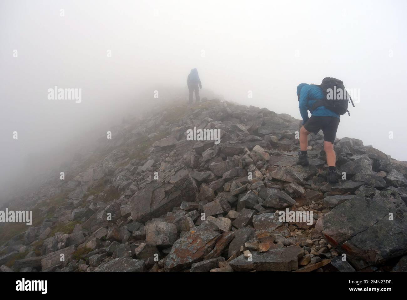 Dos hombres caminando en la nube baja en la cresta rocosa a la cumbre de la montaña escocesa Corbett 'Ben Damph' en las tierras altas escocesas, Escocia, Reino Unido. Foto de stock