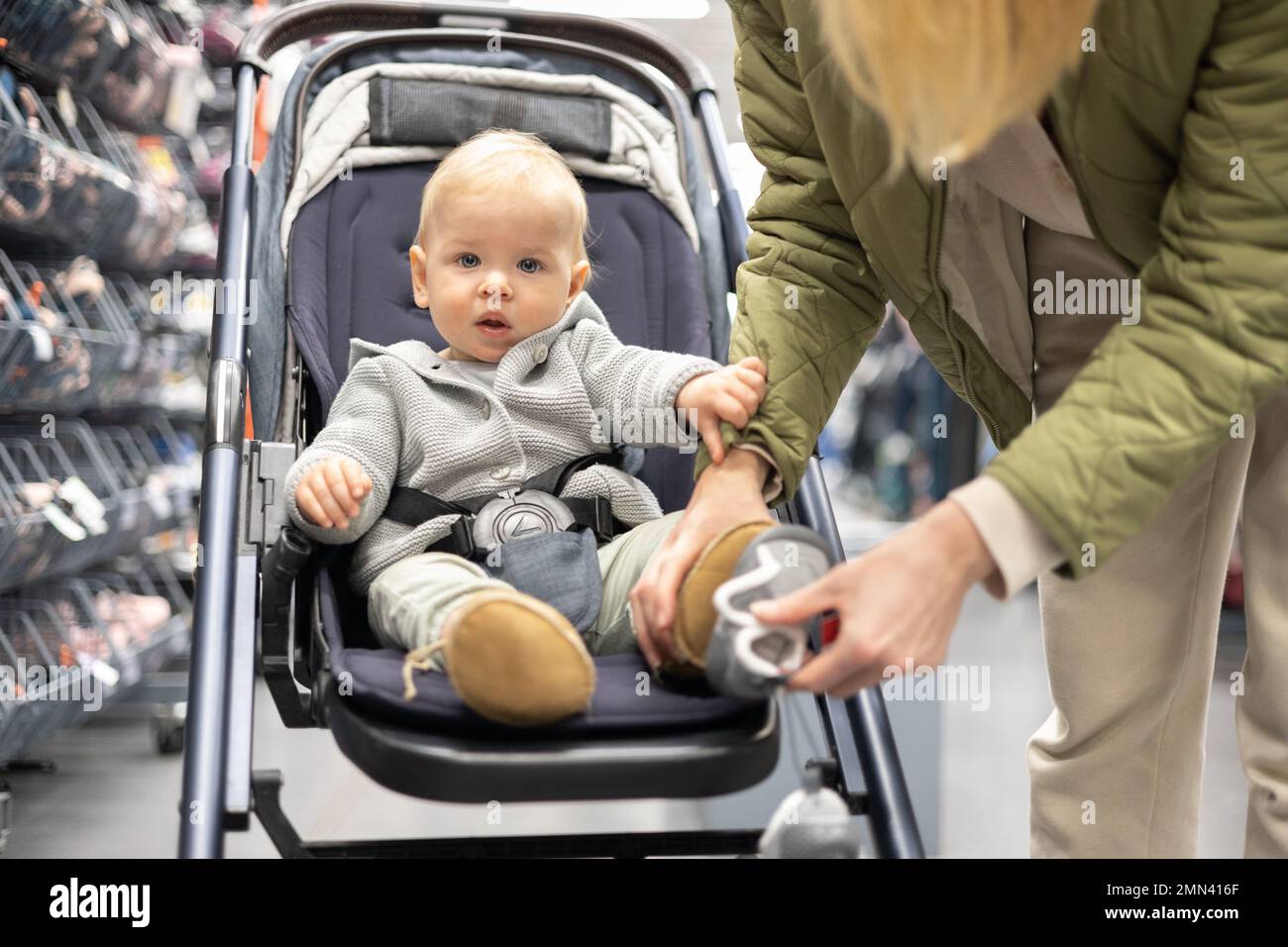 Casualy vestido madre eligiendo zapatos deportivos y productos de ropa en el departamento de deportes de la tienda del supermercado con su bebé niño en cochecito Foto de stock
