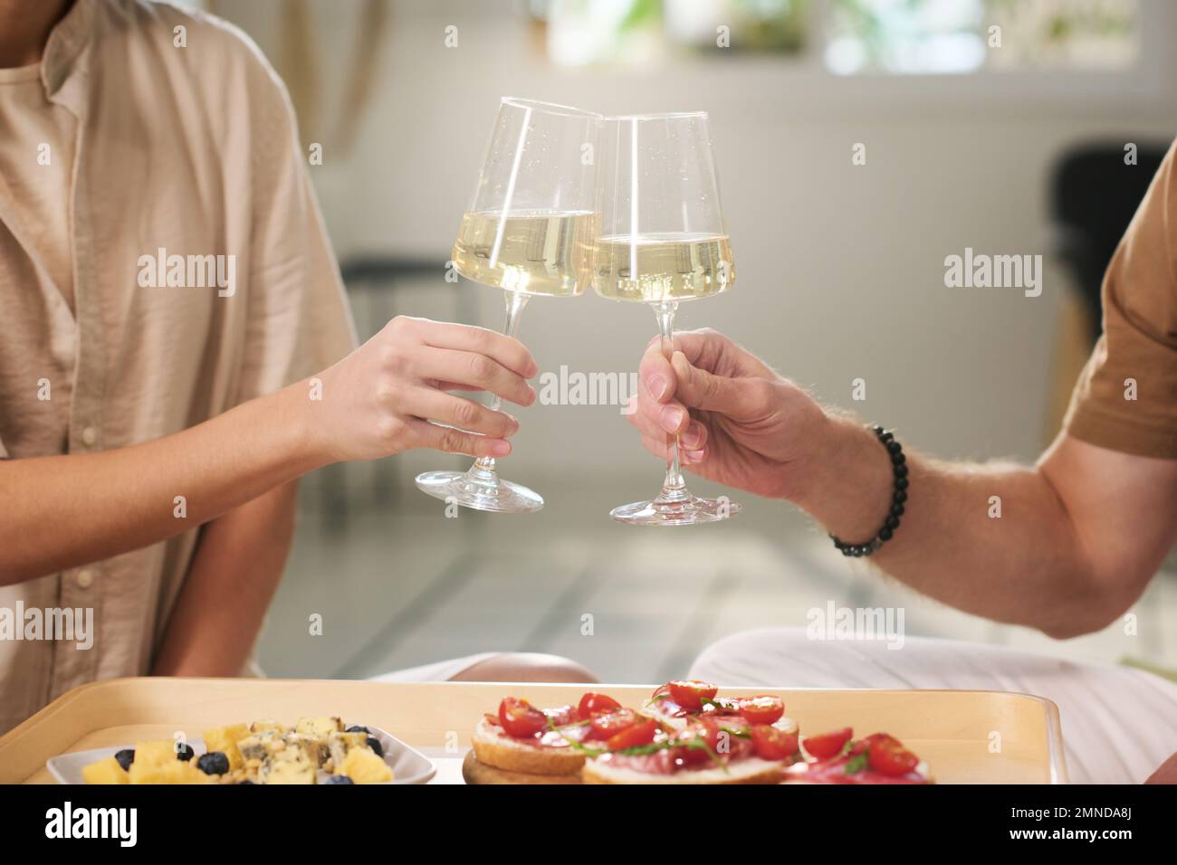 Manos de joven y mujer con flautas de champán haciendo brindis para su familia sobre bandeja con canape mientras celebran su matrimonio Foto de stock