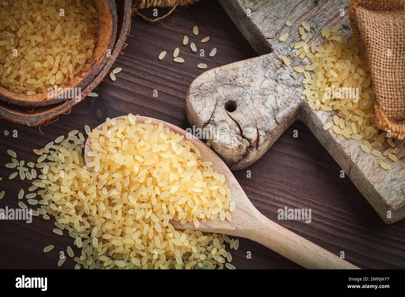 arroz marrón amarillo, utilizado para risotto en saco de arpillera yute en una tabla de cortar de madera Foto de stock