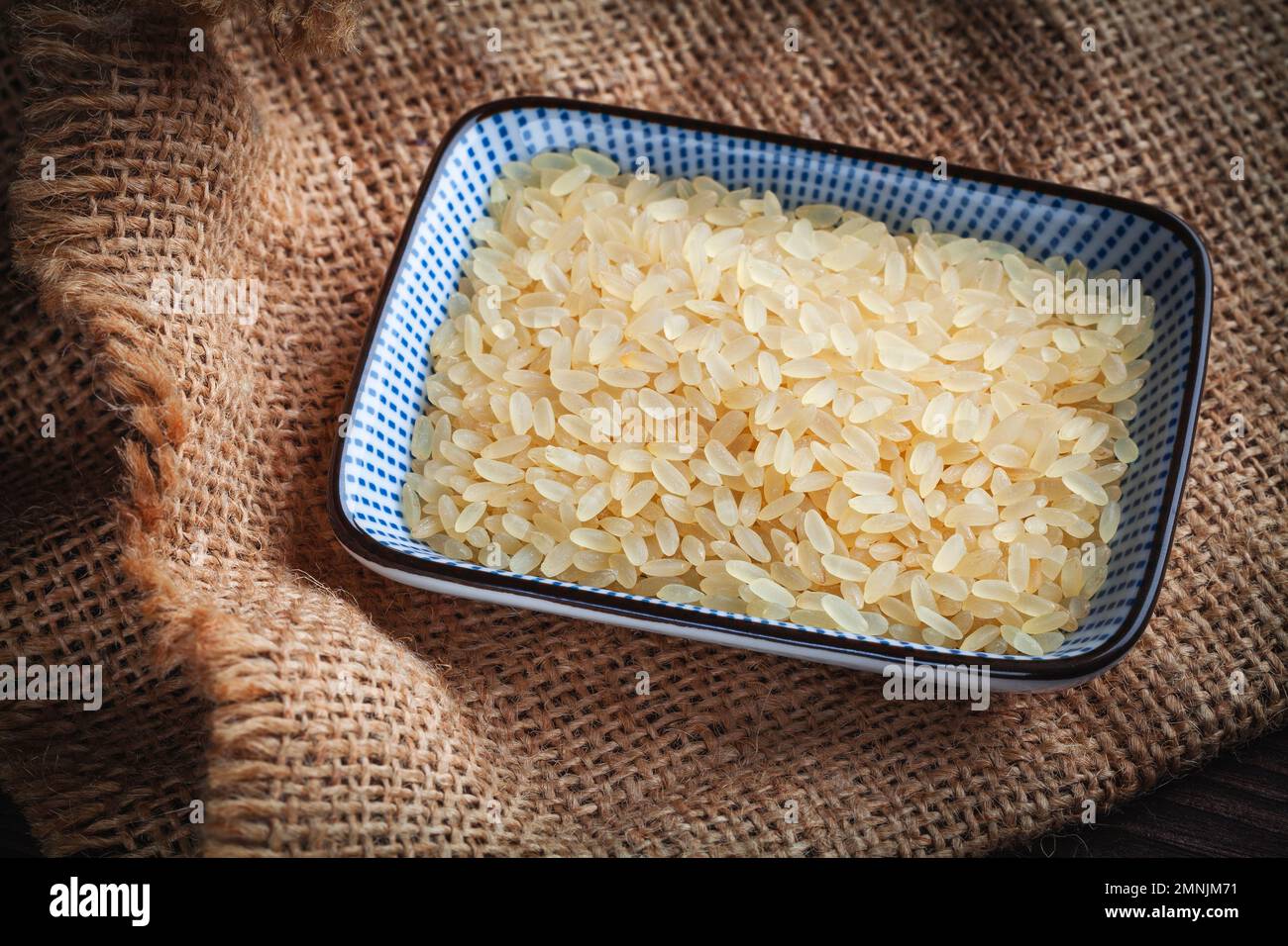 arroz integral, arroz típico para risotto, en un tazón de porcelana sobre yute Foto de stock