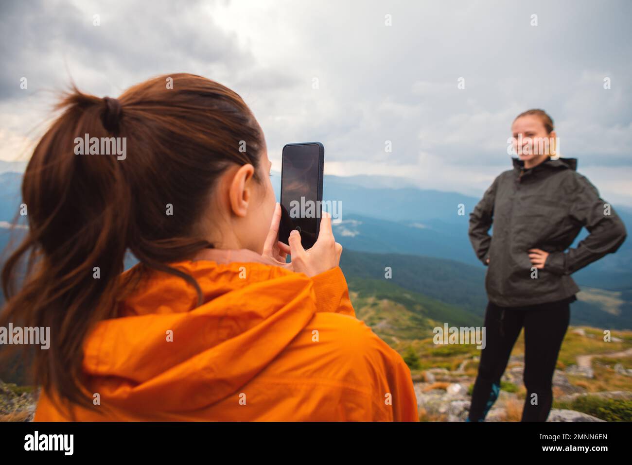 Dos amigos amigos jóvenes amigos excursionistas contra las montañas tomando una foto de un iphone en la naturaleza, Selfie teléfono inteligente moderno, usando el teléfono, amistad Foto de stock