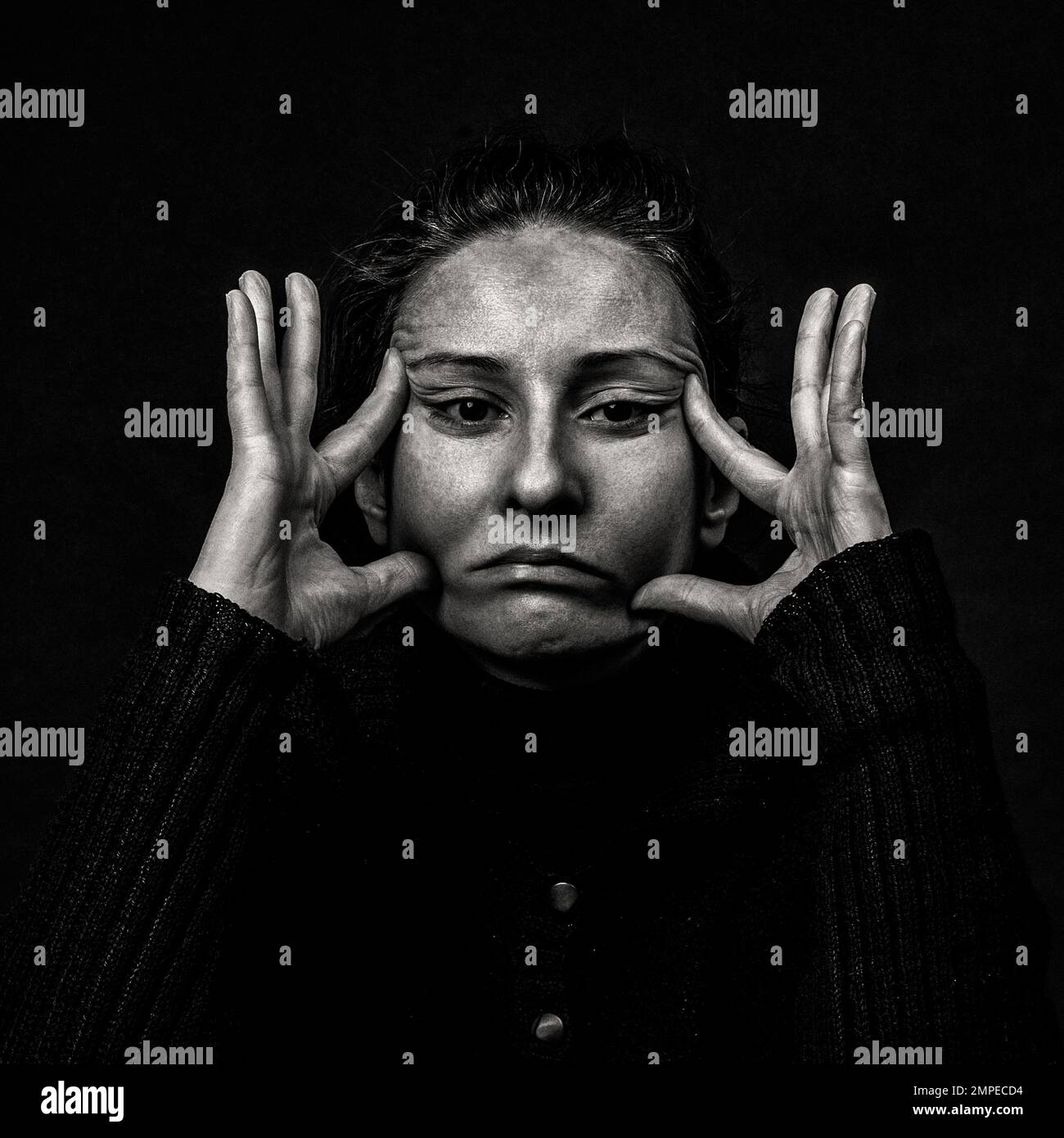 Retrato oscuro conceptual de la mujer que estira la piel de su cara en una mueca fea. Problemas con la piel y las arrugas, demostración contra el plástico sur Foto de stock