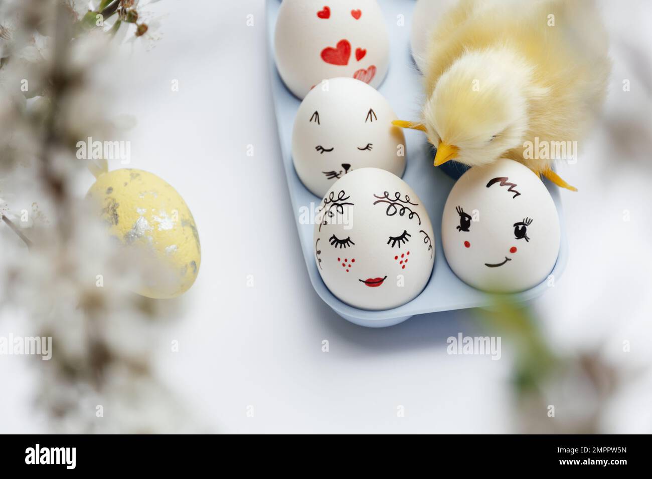 Enfoque desenfocado en primer plano. Hermosos huevos de Pascua pintados a mano en una bandeja azul. Pequeño pollo amarillo en huevos sobre fondo blanco. Concepto mínimo. Foto de stock
