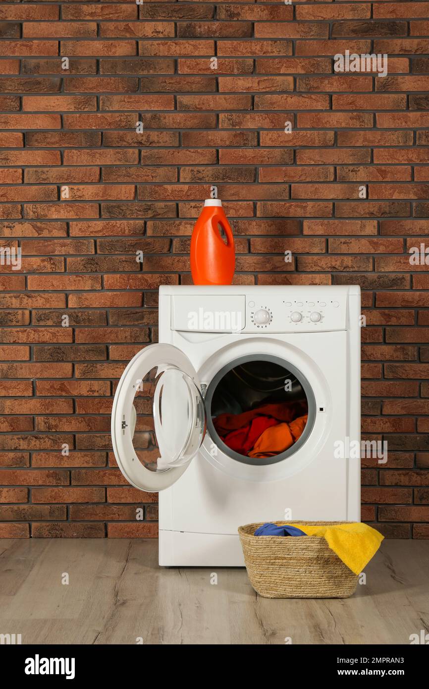 Moderna lavadora con lavandería, detergente y cesta de mimbre cerca de la  pared de ladrillo Fotografía de stock - Alamy