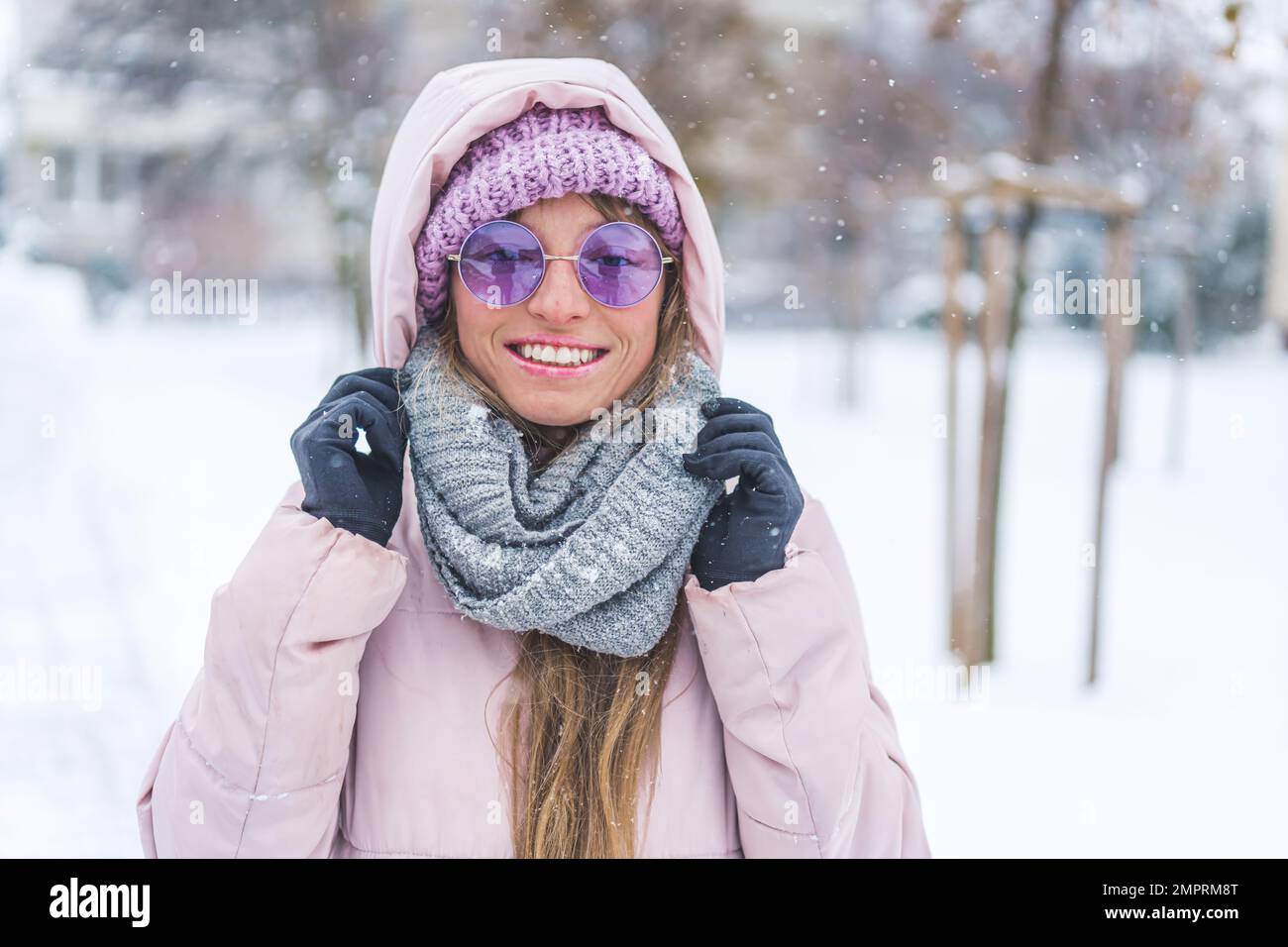 Mujer sonriente con gafas de sol y ropa de invierno de pie bajo la nieve  que cae. Foto de alta calidad Fotografía de stock - Alamy