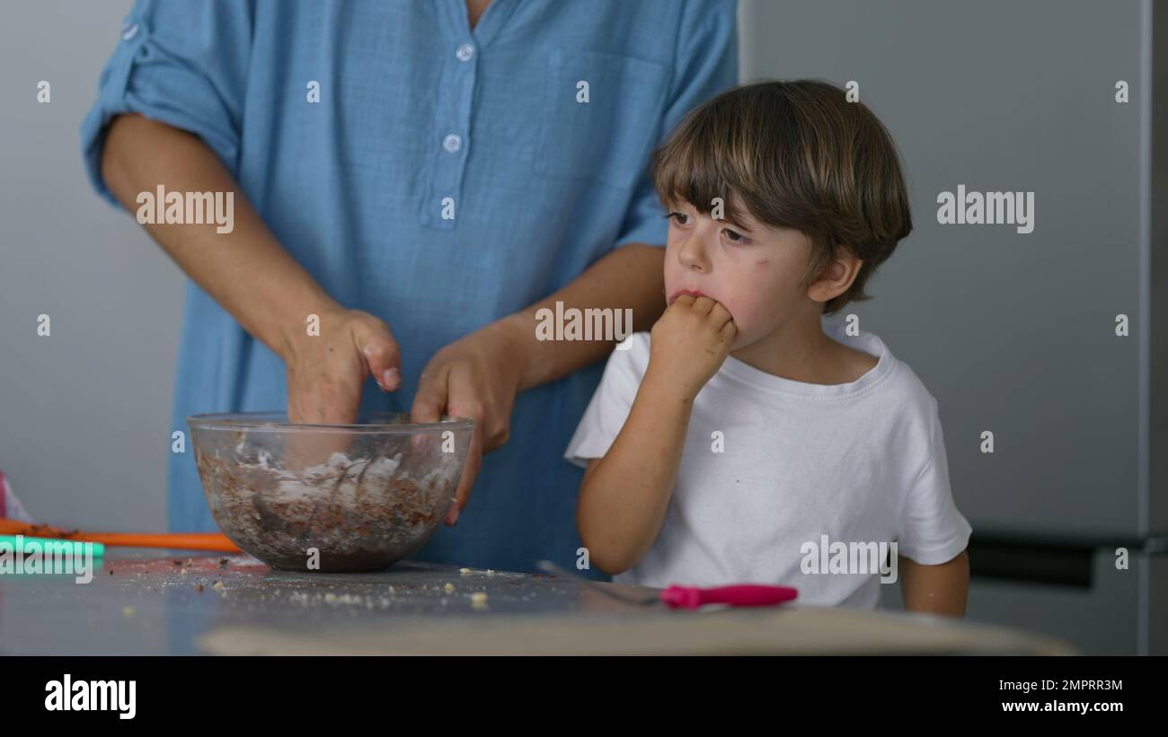 Madre mezclando ingredientes a mano con el niño comiendo masa. Padre y niño  joven preparando y horneando alimentos juntos Fotografía de stock - Alamy