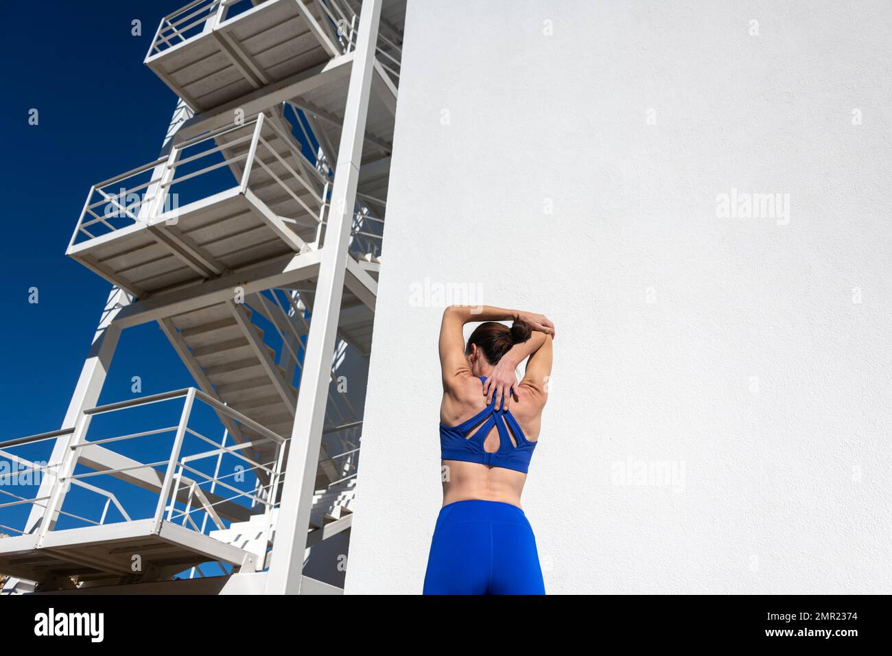 Vista trasera de una mujer deportiva haciendo un estiramiento de brazo y hombro, calentar el concepto de ejercicio. Foto de stock