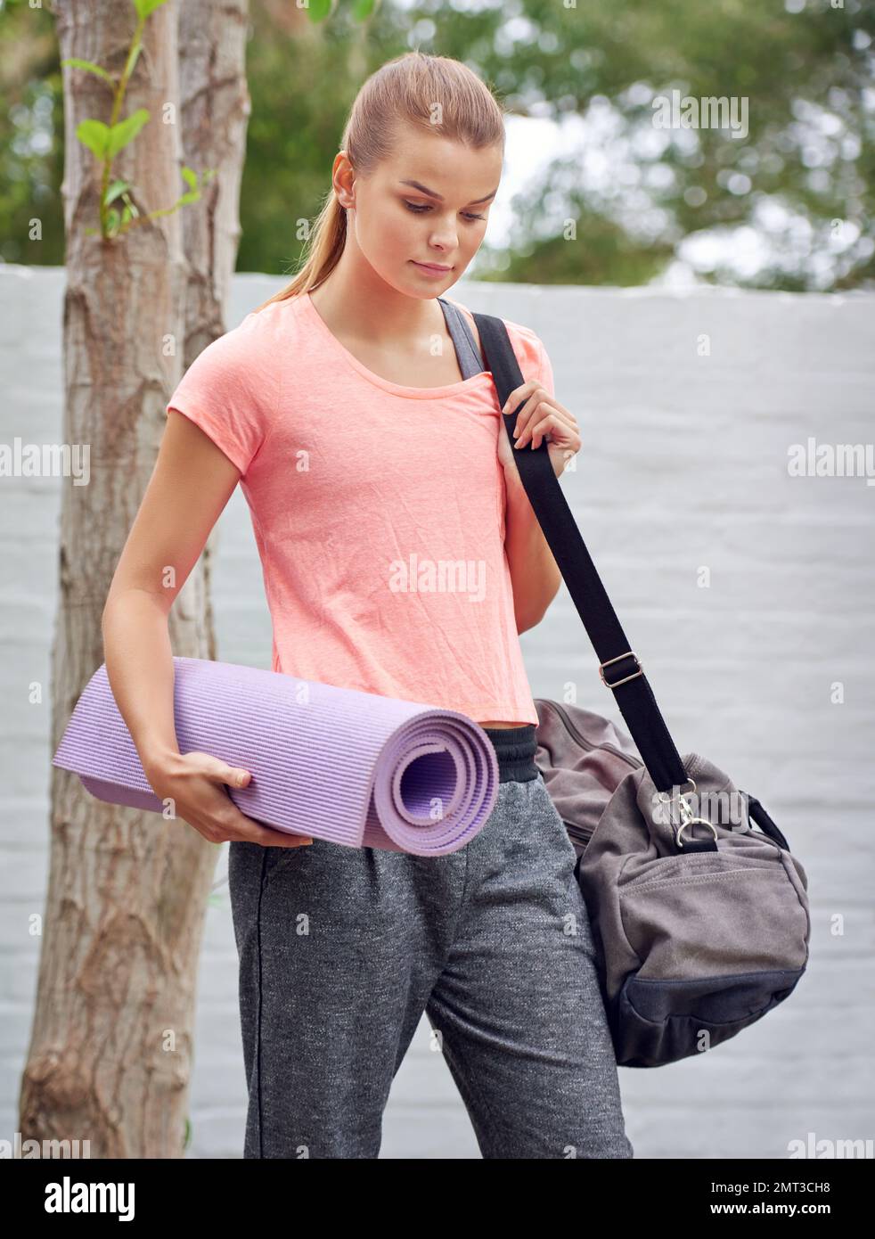 Hermosa mujer en ropa deportiva parada cerca del auto poniendo una botella  de agua en el bolso mientras va al gimnasio para entrenar