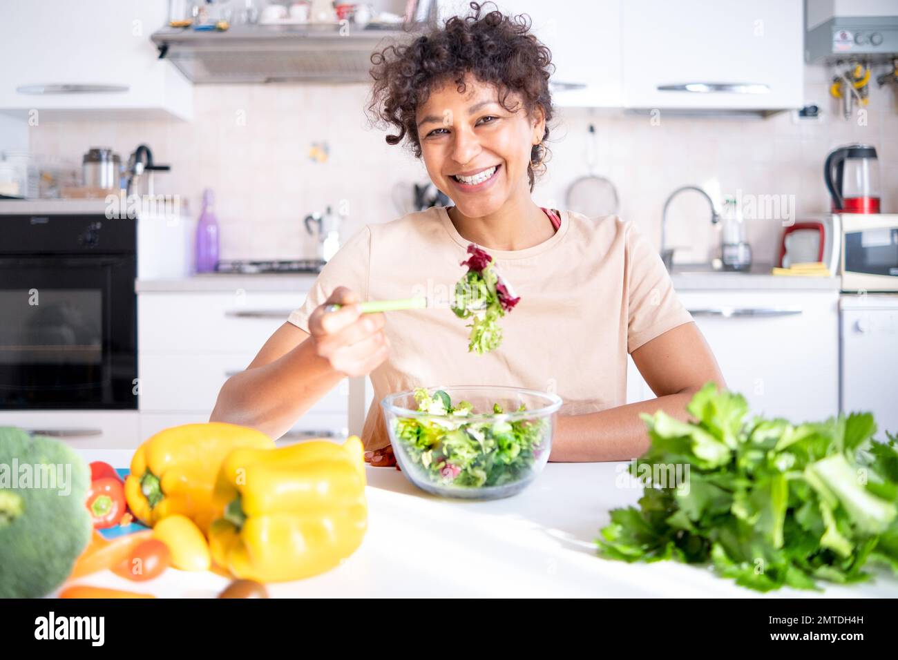 Mujer negra alegre comiendo ensalada en casa lista para la dieta Foto de stock