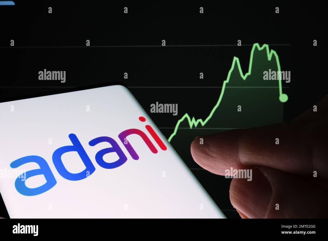 Logotipo de Adani Group visto en la pantalla del teléfono inteligente y gráfico de caída del precio de las acciones de la empresa visto en el fondo borroso. Gráfico de valores reales durante un año Foto de stock