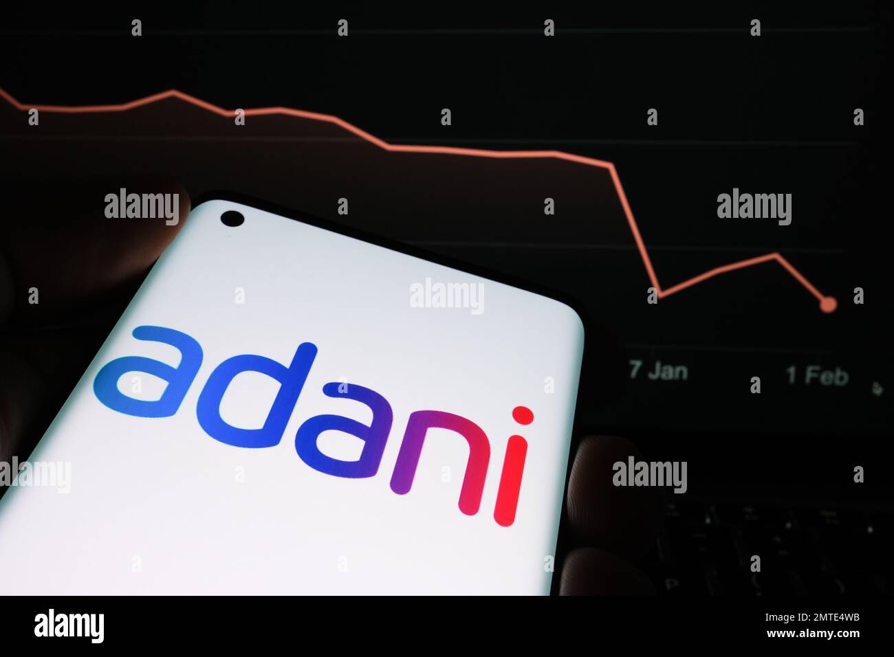 Logotipo de Adani Group visto en la pantalla del teléfono inteligente y gráfico de caída del precio de las acciones de la empresa visto en el fondo borroso. Gráfico de valores reales durante un mes Foto de stock