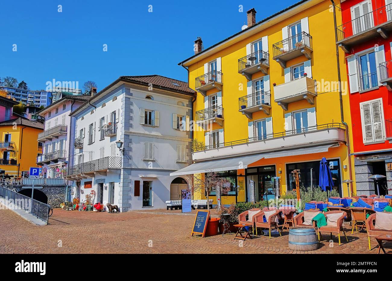 Los coloridos edificios de pequeños hoteles, restaurantes y tiendas de recuerdos dan a la Piazza Giuseppe Motta, junto al lago, en Ascona, Suiza Foto de stock