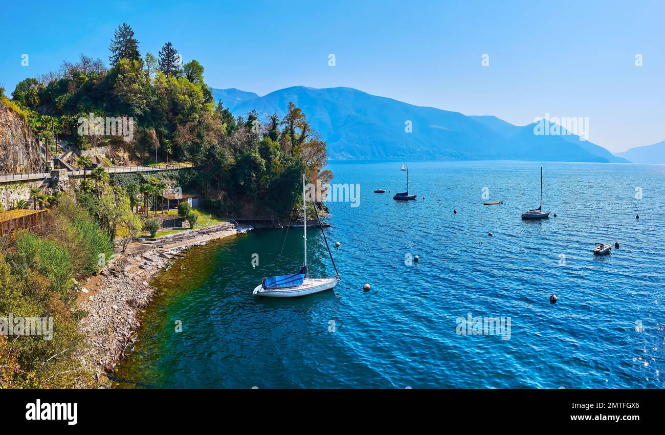 Los yates de vela amarrados contra el bosque verde en la orilla del lago Maggiore y los Alpes brumosos en el fondo, Ascona, Suiza Foto de stock