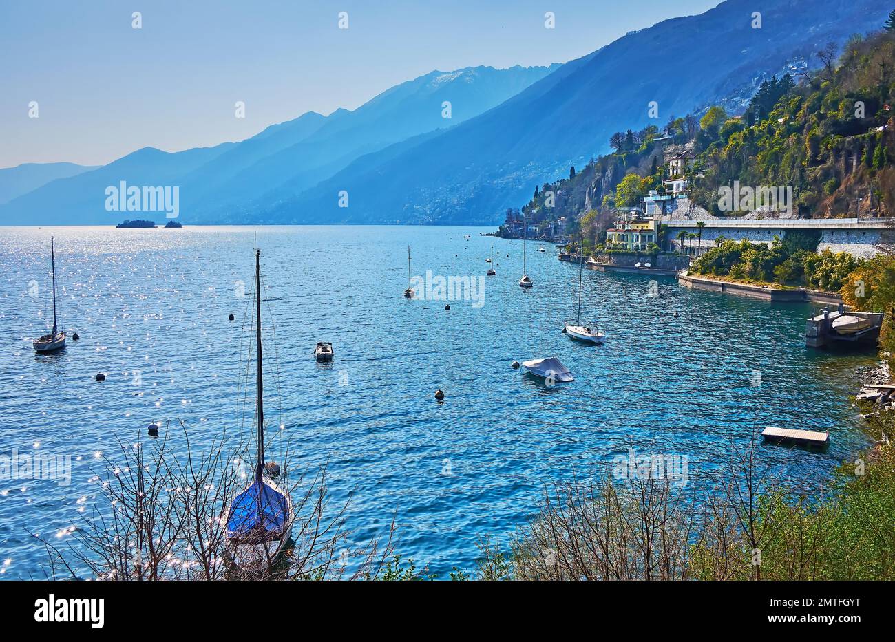 Los hermosos yates de vela en las aguas azules del lago Maggiore, rodeado de montañas nebulosas, Ascona, Suiza Foto de stock