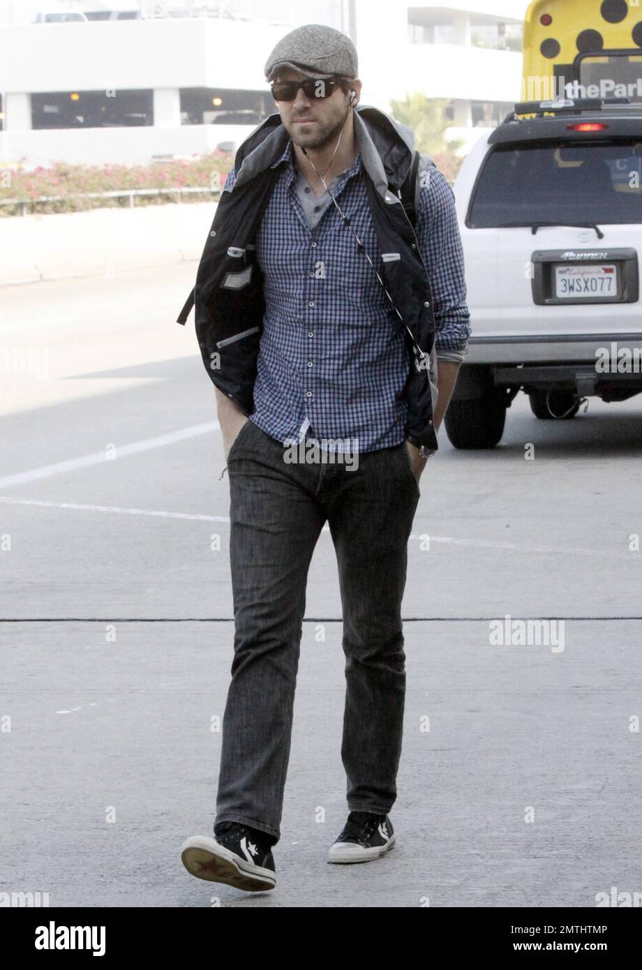 El actor Ryan Reynolds se ve casual con una camisa de cuadros, sombrero  gris y chaleco negro combinado con jeans y zapatillas negras cuando llega a  LAX después de un vuelo desde
