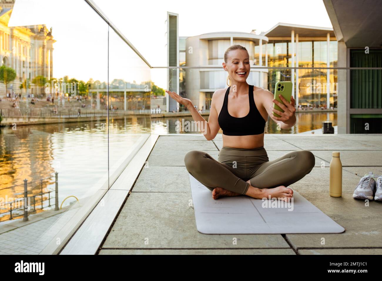 Bermad responder Verde Mujer joven blanca en chándal con teléfono móvil mientras practica yoga en  esterilla de fitness Fotografía de stock - Alamy