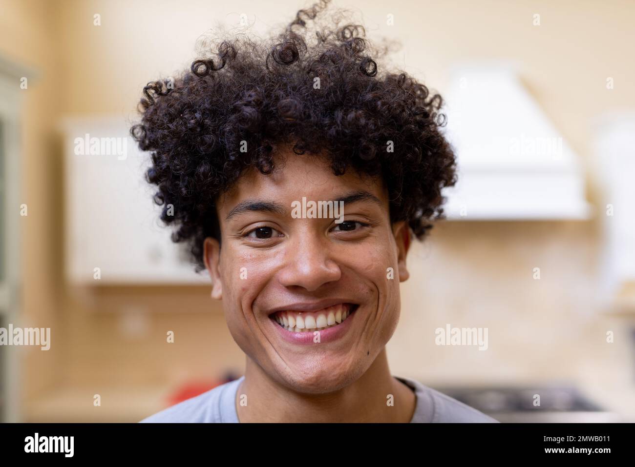 Retrato del hombre biracial sonriente con el pelo rizado en la cocina en casa Foto de stock
