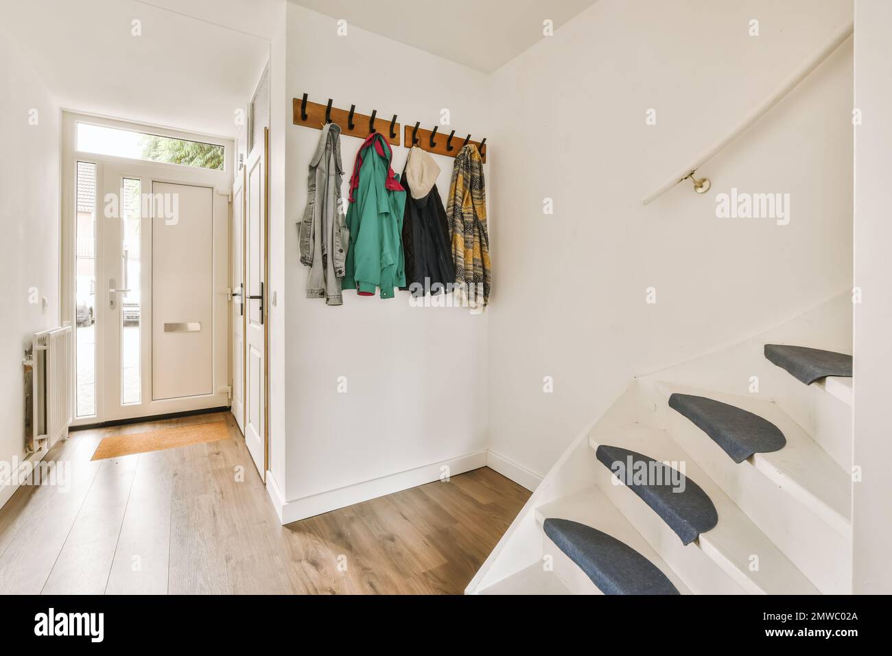 un pasillo con paredes blancas y suelos de madera hay un perchero en la  pared junto a las escaleras Fotografía de stock - Alamy