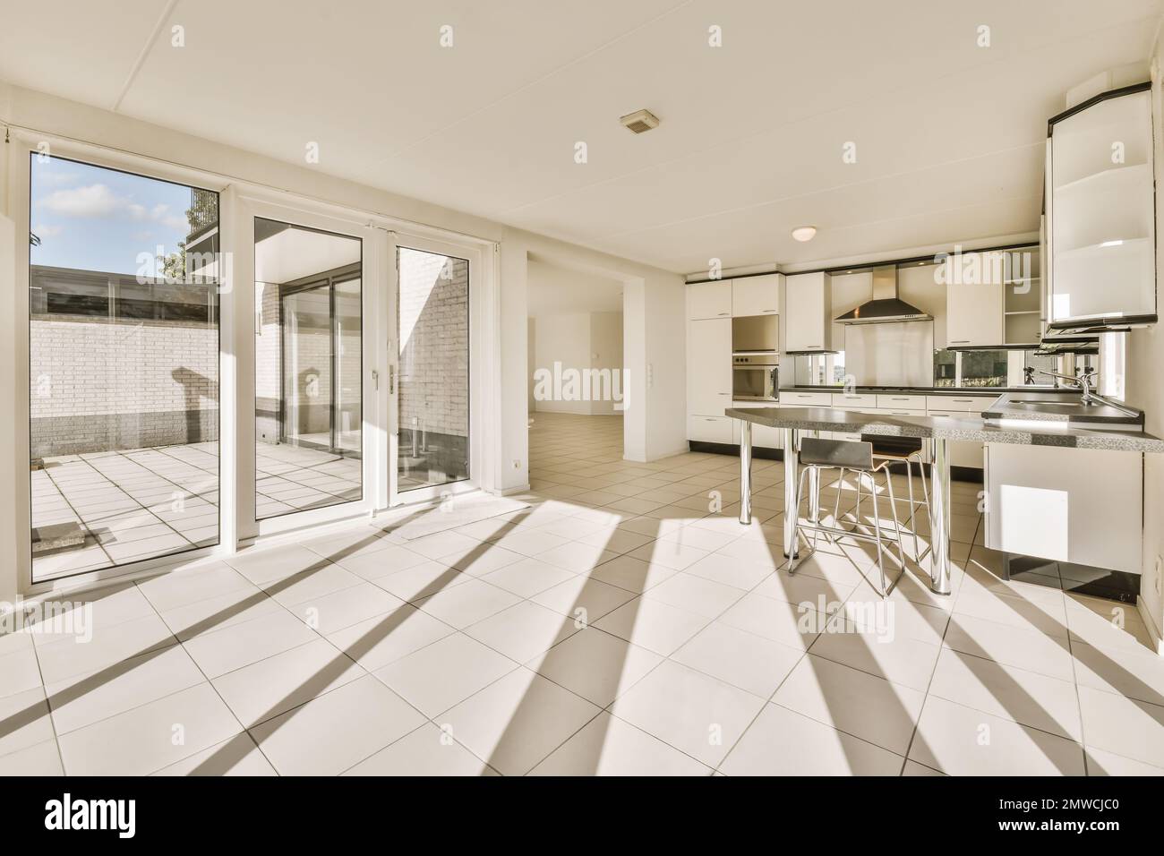 una cocina y comedor con puertas corredizas de vidrio que se abren al patio  trasero, que tiene pisos de baldosas blancas Fotografía de stock - Alamy